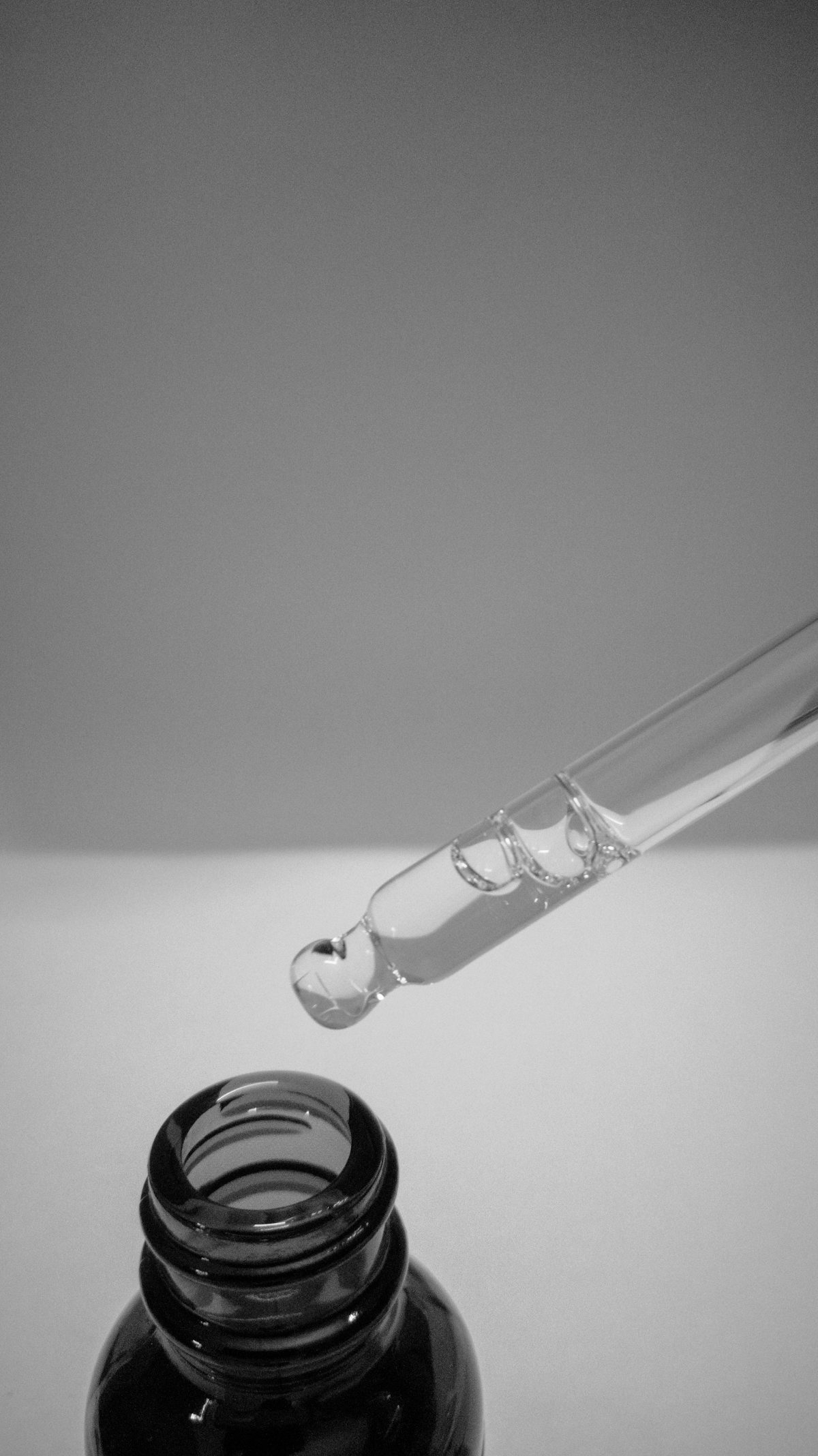 Glaspipette mit Serum vor grauem Hintergrund