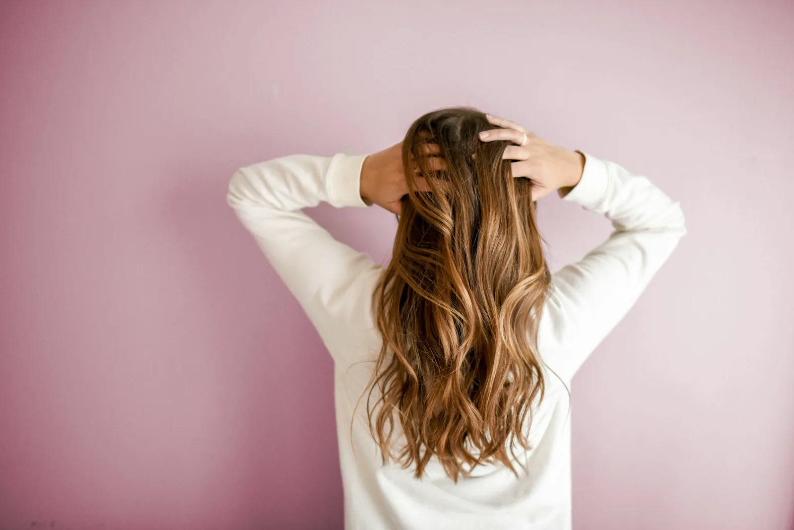 Person von hinten vor rosafarbener Wand, Hände im Haar